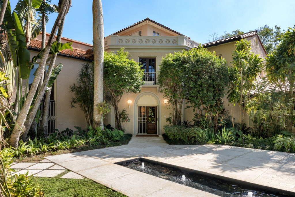 Framed by lush tropical landscaping and a serene reflecting pool, this timeless estate welcomes you with an elegant Mediterranean Revival façade.