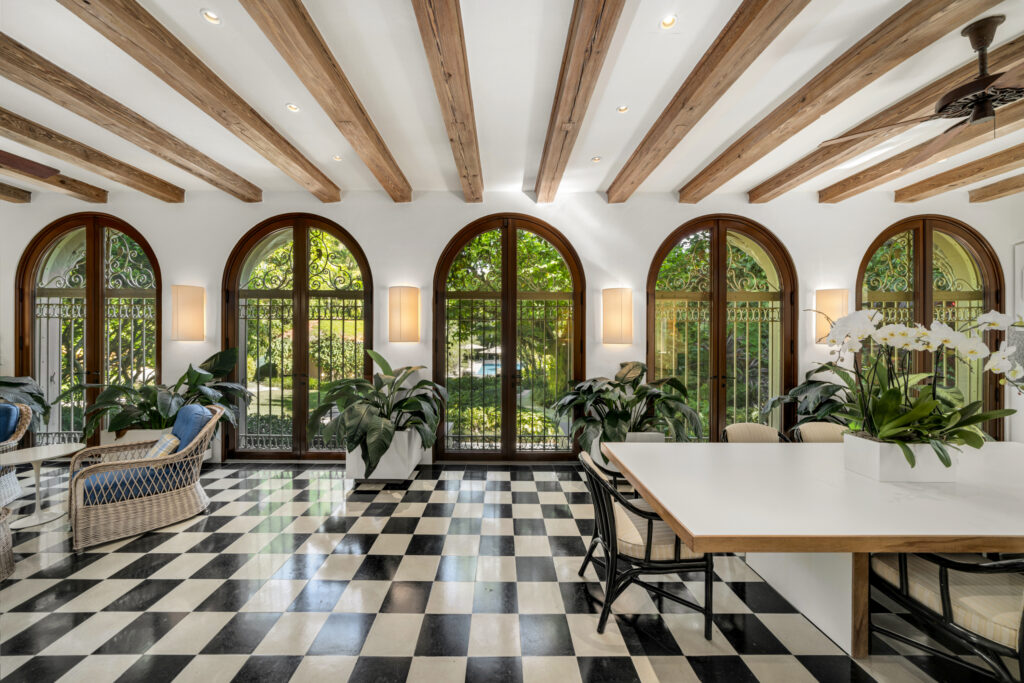 This sun-drenched lounge showcases vaulted wood-beamed ceilings, arched windows, and classic black-and-white flooring — a perfect retreat surrounded by nature.